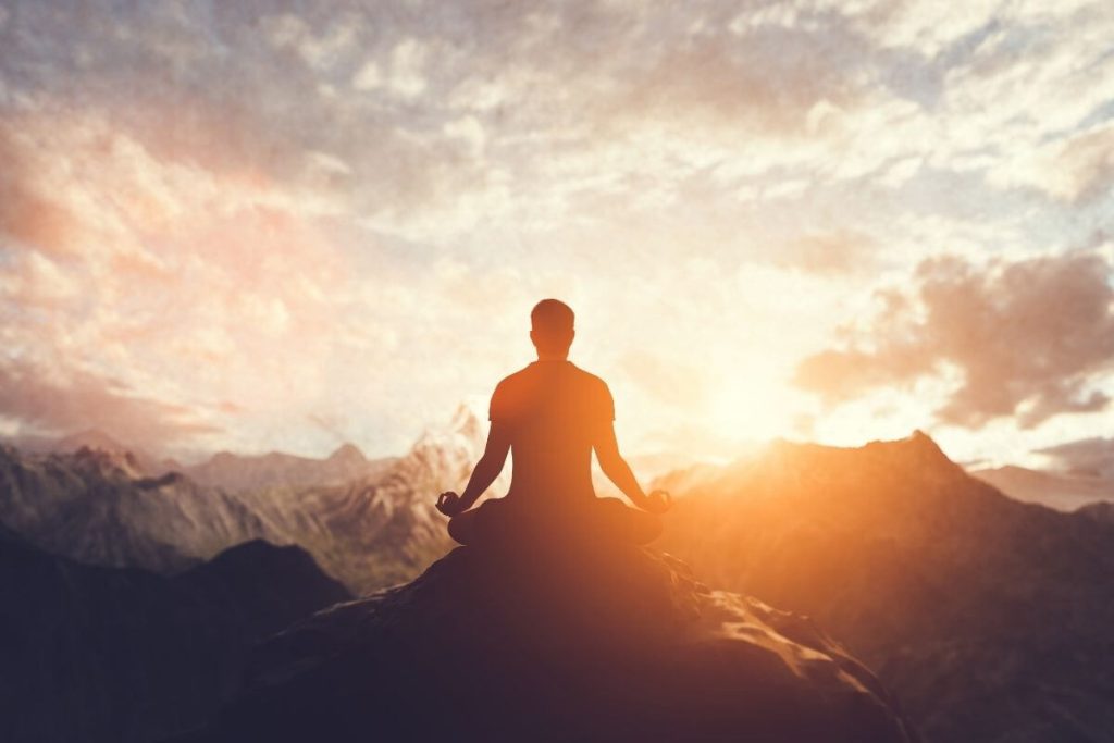 Man meditating on top of a mountain at sunrise